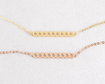 May include: Two delicate necklaces with a bar pendant featuring a row of small circles. The top necklace is gold and the bottom necklace is rose gold.