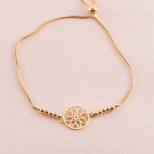 May include: A gold adjustable bracelet with a delicate chain and a circular pendant featuring a geometric design.