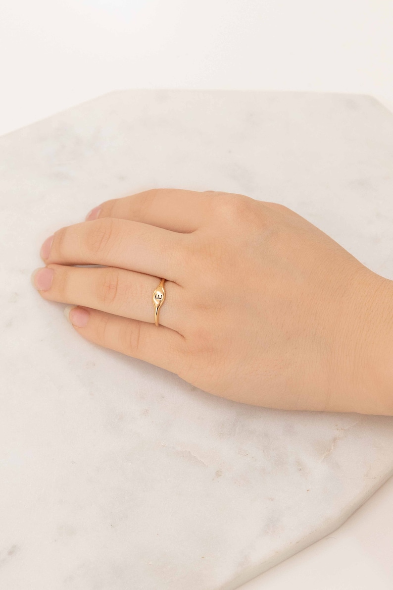 May include: A gold signet ring with the letter "E" engraved on the top. The ring is worn on a person's finger.