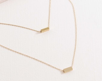 May include: A gold layered necklace with two thin chains and two small rectangular bar pendants.
