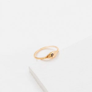May include: A gold signet ring with the letter "P" engraved on the top. The ring is on a white background.