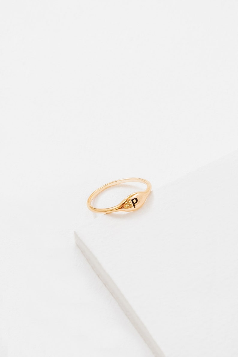 May include: A gold signet ring with the letter "P" engraved on the top. The ring is on a white background.