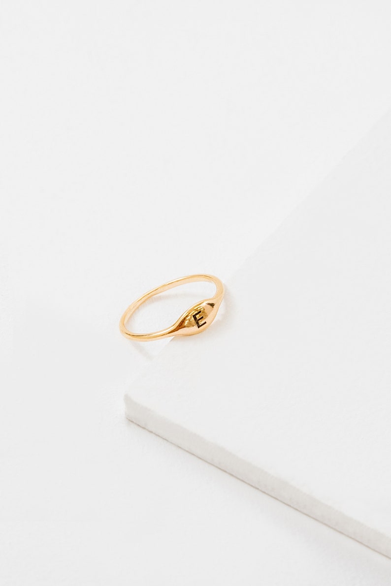 May include: A gold signet ring with the letter "E" engraved on the top.