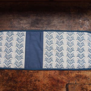 Könnte beinhalten: Ein rechteckiger Ofenhandschuh mit blau-weißem Blumenmuster. Der Handschuh hat ein durchgehend blaues Mittelteil und einen blauen Rand. Das florale Design ist ein sich wiederholendes Muster aus stilisierten Blättern.