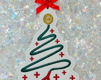 May include: White Christmas tree ornament with a green tree design, red crosses, and a stethoscope. The ornament has a red ribbon and bow at the top. The ornament is approximately 4 inches tall.