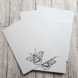 Pode incluir: Um conjunto de três cartões brancos em branco com uma ilustração em preto e branco de uma abelha na frente.