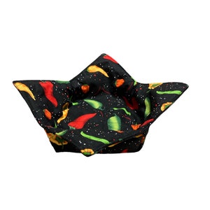 May include: A black fabric bowl with a red, yellow, and green chili pepper pattern. The bowl is folded and ready to be used.