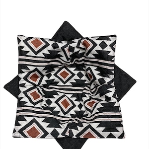May include: A black and white geometric patterned fabric with brown accents. The fabric is folded into a square shape.