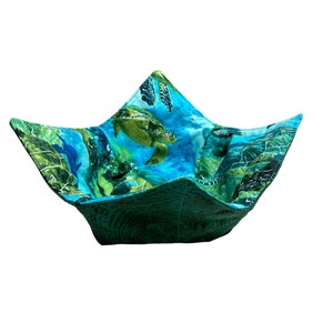 May include: A teal blue fabric bowl with a green and blue sea turtle print. The bowl is folded into a star shape.