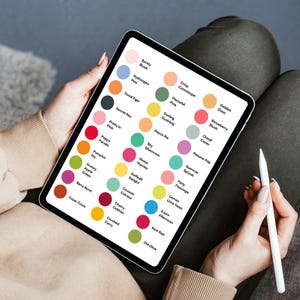 May include: A tablet displaying a color palette with various hues and names, including "Barely Blush," "Hydrangea Hue," and "Crisp Cantaloupe." A white stylus rests on the side. The tablet is held by a person.
