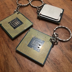 May include: Three silver keychains with a gold-colored CPU chip attached to each. The chips have a grid pattern and small black squares.