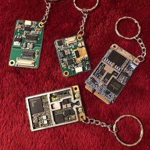 Può includere: Quattro piccole schede a circuito stampato con portachiavi argentati. Le schede a circuito stampato sono verdi e blu con vari componenti elettronici.