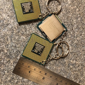 May include: Two computer processor chips on a silver keychain. The chips are green and gold with text that reads "Intel Pentium SR18A 2.0GHz Malay 1". A silver ruler is in the bottom of the image.