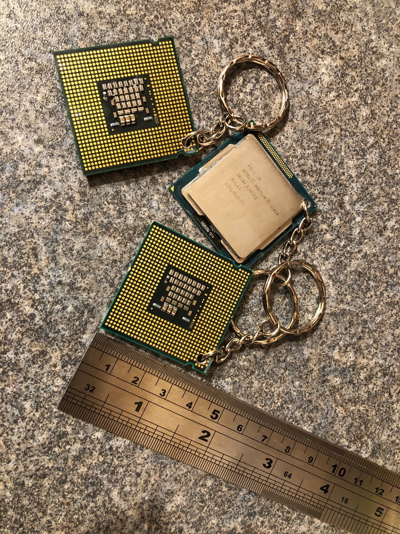May include: Two computer processor chips on a silver keychain. The chips are green and gold with text that reads "Intel Pentium SR18A 2.0GHz Malay 1". A silver ruler is in the bottom of the image.