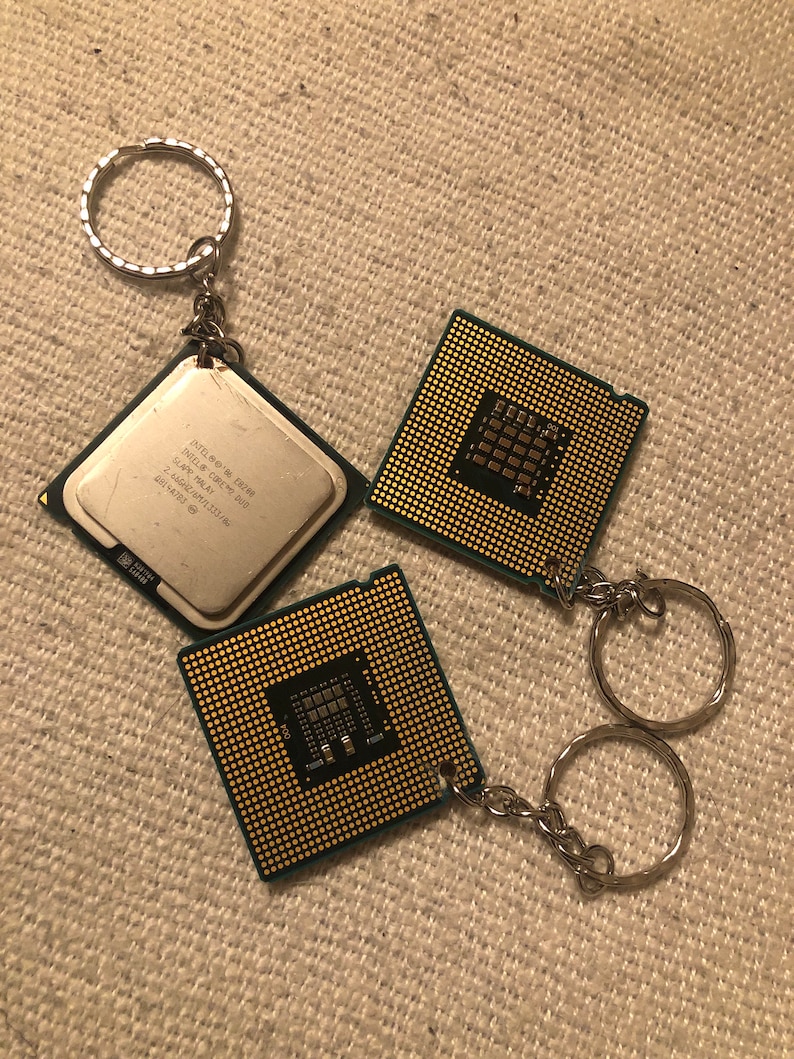 May include: Two gold-colored computer chip keychains with silver key rings. The chips have a green circuit board design and the text "Intel Core i7 CPU" is visible on one of the chips.