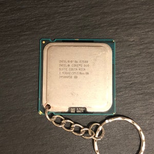 May include: A silver keychain with a small silver chain and a silver ring. The keychain features a silver square with the text "INTEL&reg; '06 E7500 INTEL&reg; CORE&trade;2 DUO SLGTE COSTA RICA 2.93GHZ/3M/1066/06 3958A858" printed on it.