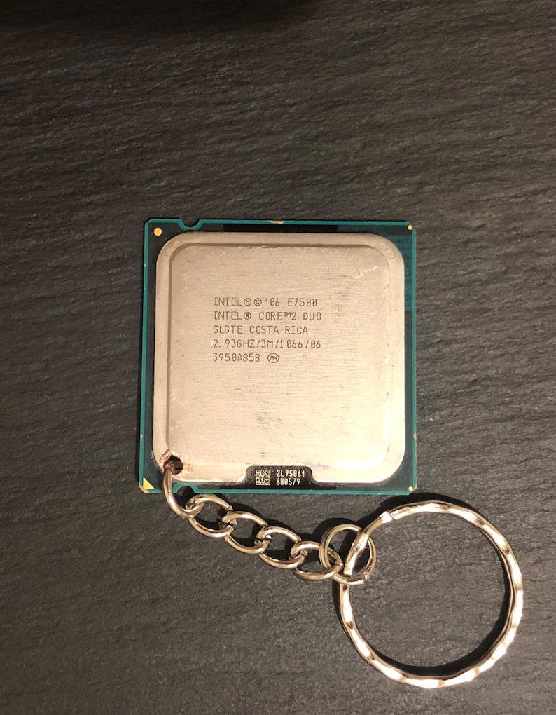May include: A silver keychain with a small silver chain and a silver ring. The keychain features a silver square with the text "INTEL&reg; '06 E7500 INTEL&reg; CORE&trade;2 DUO SLGTE COSTA RICA 2.93GHZ/3M/1066/06 3958A858" printed on it.