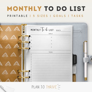 May include: A white monthly planner with a gold binder ring. The planner has sections for goals, tasks, modules, courses, and yearly. The planner is open to a page with the text "MONTHLY To do LIST" and "PLAN TO THRIVE".