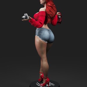 May include: A figurine of a woman with long red hair, wearing a red off-the-shoulder top, denim shorts, and red high heels. She holds a silver camera and stands on a black base with a white design.