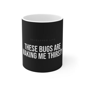 May include: Black ceramic mug with the text "THESE BUGS ARE MAKING ME THIRSTY" in white, under the words "DEVELOPER LIFE". The mug has a white interior.