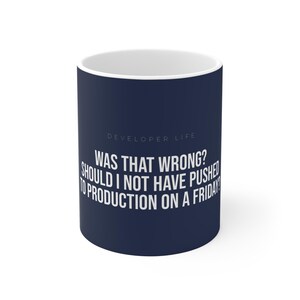 May include: A white ceramic mug with a navy blue exterior. The mug features the text "DEVELOPER LIFE" above the question: "WAS THAT WRONG? SHOULD I NOT HAVE PUSHED TO PRODUCTION ON A FRIDAY?" in white lettering.