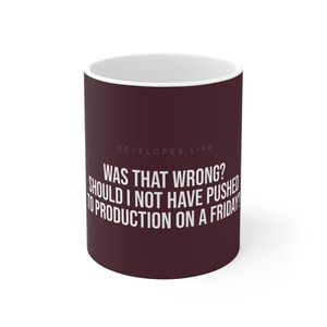 May include: A maroon coffee mug with the text "DEVELOPER LIFE" and the question "WAS THAT WRONG? SHOULD I NOT HAVE PUSHED TO PRODUCTION ON A FRIDAY?" in white. The mug has a white interior.