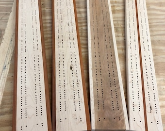 May include: Four wooden cribbage boards with maple and mahogany wood. Each board has a different wood grain pattern.
