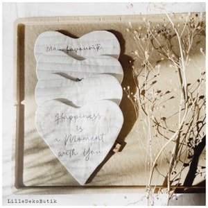 May include: Three white quilted heart-shaped pillows with black embroidered text. The top pillow says "My favourite", the middle pillow is blank, and the bottom pillow says "Happiness is a moment with you".