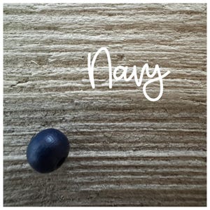 May include: A single, dark blue wooden bead on a woodgrain background. The word "Navy" is written in white above the bead.