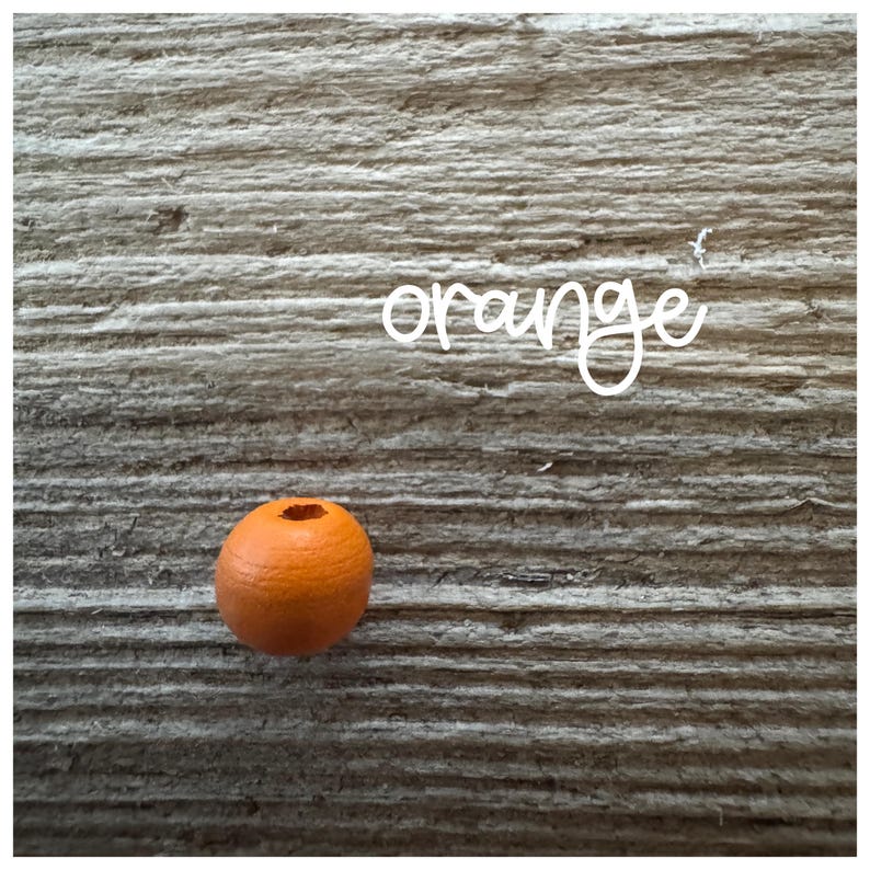 May include: A single orange wooden bead on a woodgrain background. The word "orange" is written in white above the bead.