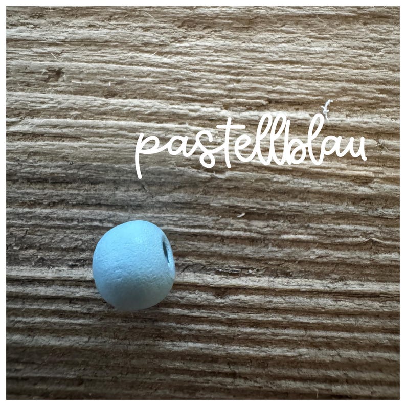 May include: A single light blue wooden bead on a wood background. The word "pastellblau" is written in white on the wood.