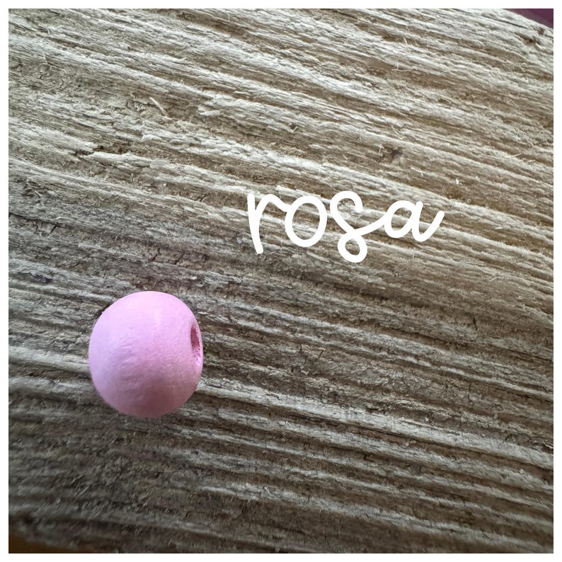 May include: A single pink wooden bead on a wood background. The word "rosa" is written in white above the bead.