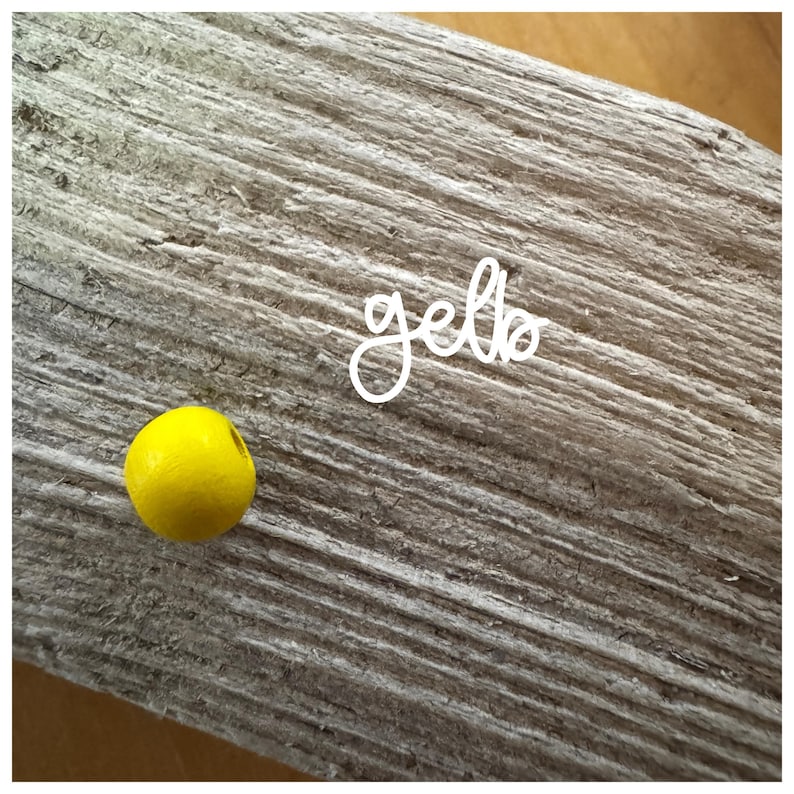 May include: A single yellow wooden bead on a light brown wooden surface with the word "gello" written in white cursive.