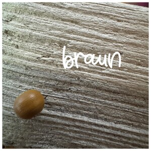 May include: A close-up of a light brown wooden surface with the word "braun" written in white. A small, round, light brown object is in the lower left corner of the image.
