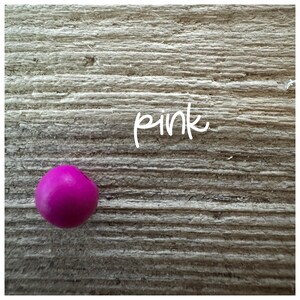 May include: A single pink bead on a wood background with the word "pink" written in white.