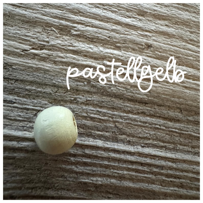 May include: A single, round, wooden bead in a pale pastel yellow color. The bead is on a woodgrain background.