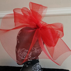 May include: A large red tulle bow with a sheer veil attached. The bow is made of soft, delicate fabric and is perfect for adding a touch of elegance to any outfit.