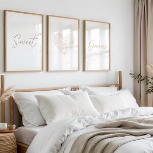 May include: A bedroom with a bed dressed in white bedding and pillows, with a beige throw. Above the bed are three framed prints with the words "Sweet" and "Dreams", and a heart design. The room has a neutral colour palette.