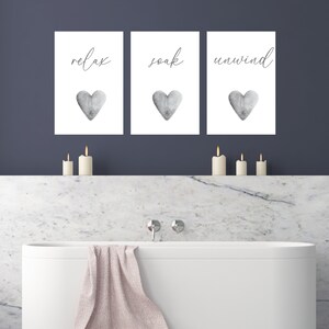 May include: Three white framed prints with black text and gray watercolor hearts. The prints read "relax", "soak", and "unwind".
