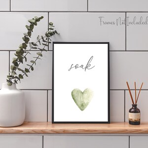 May include: A white printable art print with a black frame. The print features a green watercolor heart and the word "soak" in gray cursive writing.