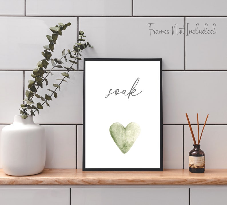 May include: A white printable art print with a black frame. The print features a green watercolor heart and the word "soak" in gray cursive writing.