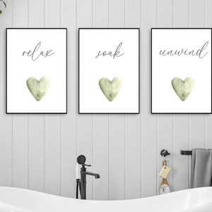 May include: Three framed prints with white backgrounds and black frames. Each print features a green watercolor heart and a handwritten word: "relax", "soak", and "unwind".
