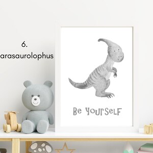 Puede incluir: Una ilustraci&oacute;n de acuarela en blanco y negro de un dinosaurio Parasaurolophus con el texto "Be Yourself" sobre un fondo blanco. La ilustraci&oacute;n est&aacute; enmarcada y se muestra en un estante con un oso de peluche gris y otros art&iacute;culos decorativos.