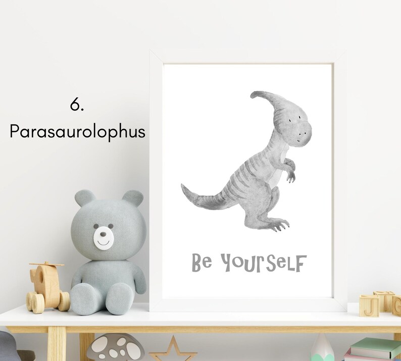 Puede incluir: Una ilustraci&oacute;n de acuarela en blanco y negro de un dinosaurio Parasaurolophus con el texto "Be Yourself" sobre un fondo blanco. La ilustraci&oacute;n est&aacute; enmarcada y se muestra en un estante con un oso de peluche gris y otros art&iacute;culos decorativos.