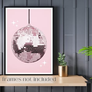 May include: A pink and silver disco ball hanging from the ceiling against a pink background. The disco ball has a shiny, mirrored surface with small squares. There are small white stars on the background.