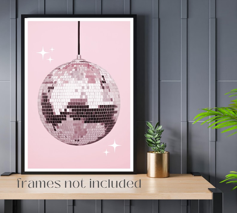 May include: A pink and silver disco ball hanging from the ceiling against a pink background. The disco ball has a shiny, mirrored surface with small squares. There are small white stars on the background.