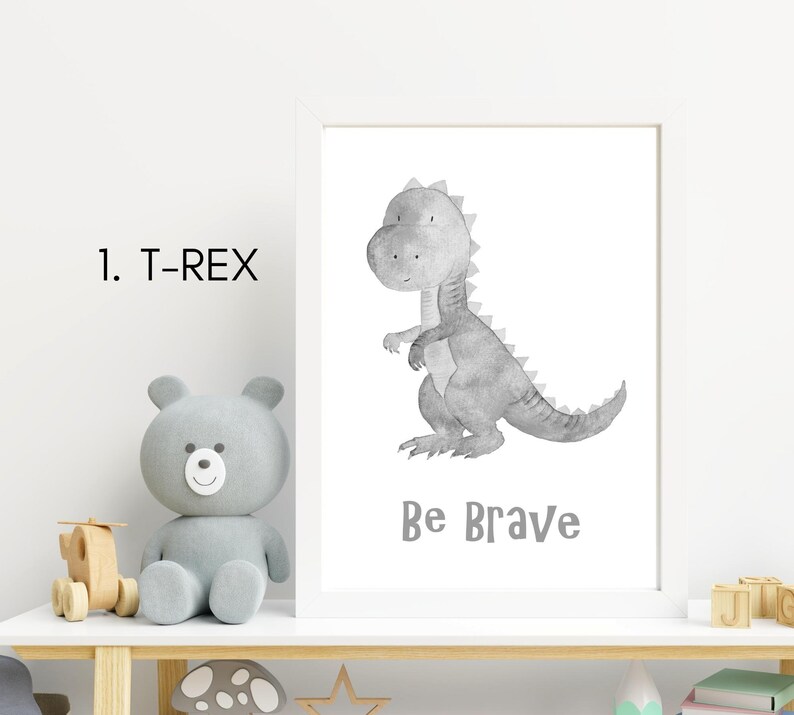 Puede incluir: Una ilustraci&oacute;n de acuarela en blanco y negro de un dinosaurio T-Rex con el texto "Be Brave" debajo. La ilustraci&oacute;n est&aacute; enmarcada en un marco blanco y est&aacute; sentada en un estante blanco.