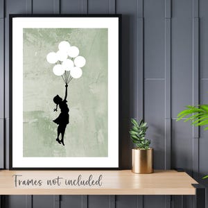 May include: A black silhouette of a person holding white balloons against a green textured background. The image is framed in black.