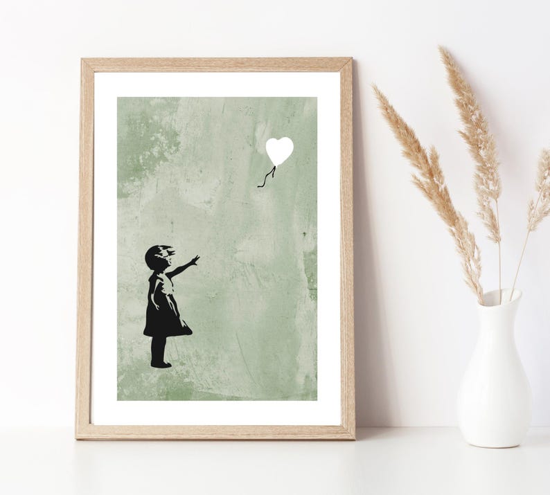 May include: A black and white print of a girl reaching for a white heart-shaped balloon. The background is a green textured wall.