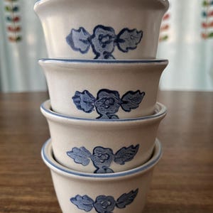 May include: A stack of four off-white ceramic bowls with a blue floral design. Each bowl has a blue rim and a matching floral pattern. The bowls are stacked on top of each other, showcasing the design.